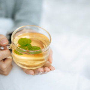 A person holding a warm herbal tea cup with mint, promoting post-tongue scraping hydration for oral and digestive health