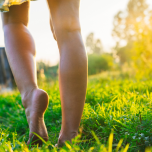 A person walking barefoot on grass with soft sunlight, grounding energy to calm Pitta dosha.