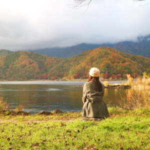 A serene scene of a person sitting near a lake with mountains in the background, symbolizing the soothing effect of nature on Pitta energy.