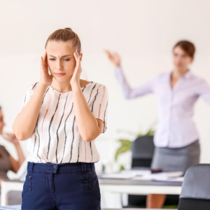 A stressed woman holding her head while someone in the background is arguing, reflecting irritability and mental imbalance of Pitta dosha.