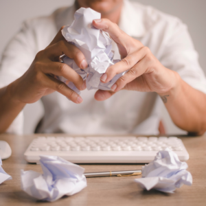 Hands crushing paper in frustration, symbolizing perfectionism and overwhelm caused by an imbalanced Pitta dosha.