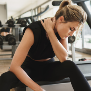 An exhausted woman sitting at the gym, representing physical burnout from overexertion, a sign of excess Pitta energy.