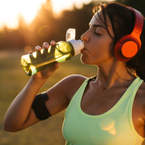 A woman drinking water outdoors while wearing headphones, emphasizing hydration to cool down Pitta energy.