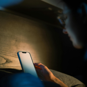 A person scrolling on their phone in a dark room, representing the need to limit screen time before bed to soothe Pitta.