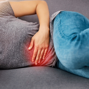 Woman lying in bed holding her stomach, suffering from inflammation and discomfort.