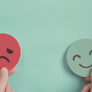Two hand-held emoji faces, one sad and one happy, representing mood swings and emotional changes due to inflammation.