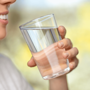 Person drinking a glass of warm water to support digestion and detox.