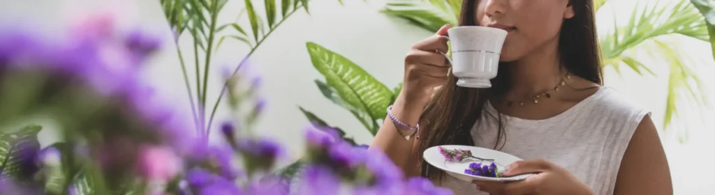 A serene woman sipping tea in a light-filled space with flowers, symbolizing calm, Ayurveda wellness, and relief from stress and inflammation.