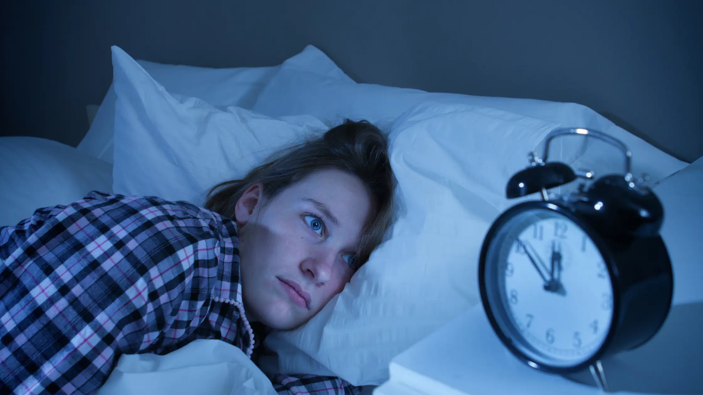 Woman lying awake in bed at night, pale moonlight through a window, eyes open and still, representing inflammation-driven sleep disruption